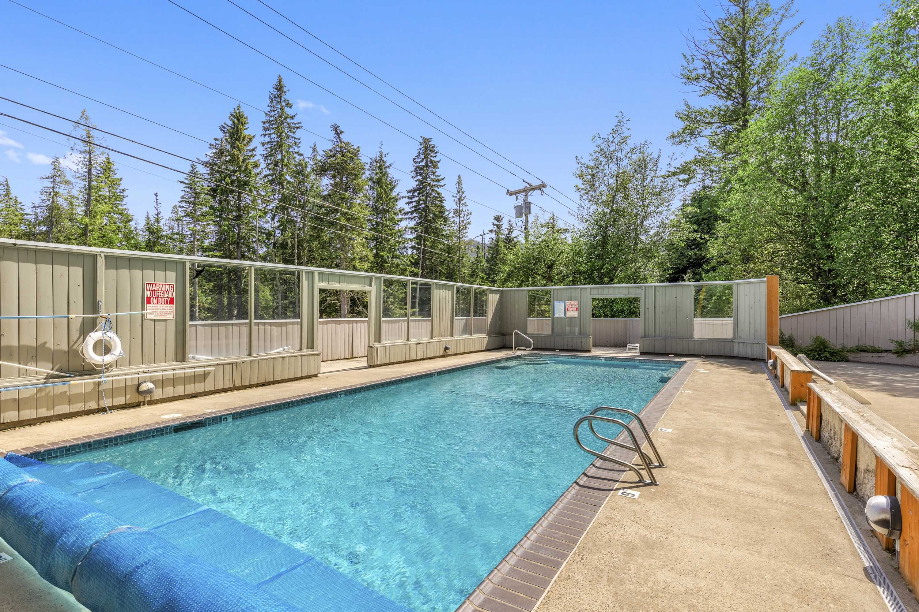 A swimming pool with a wooden deck, a lifeguard chair, and a warning sign.