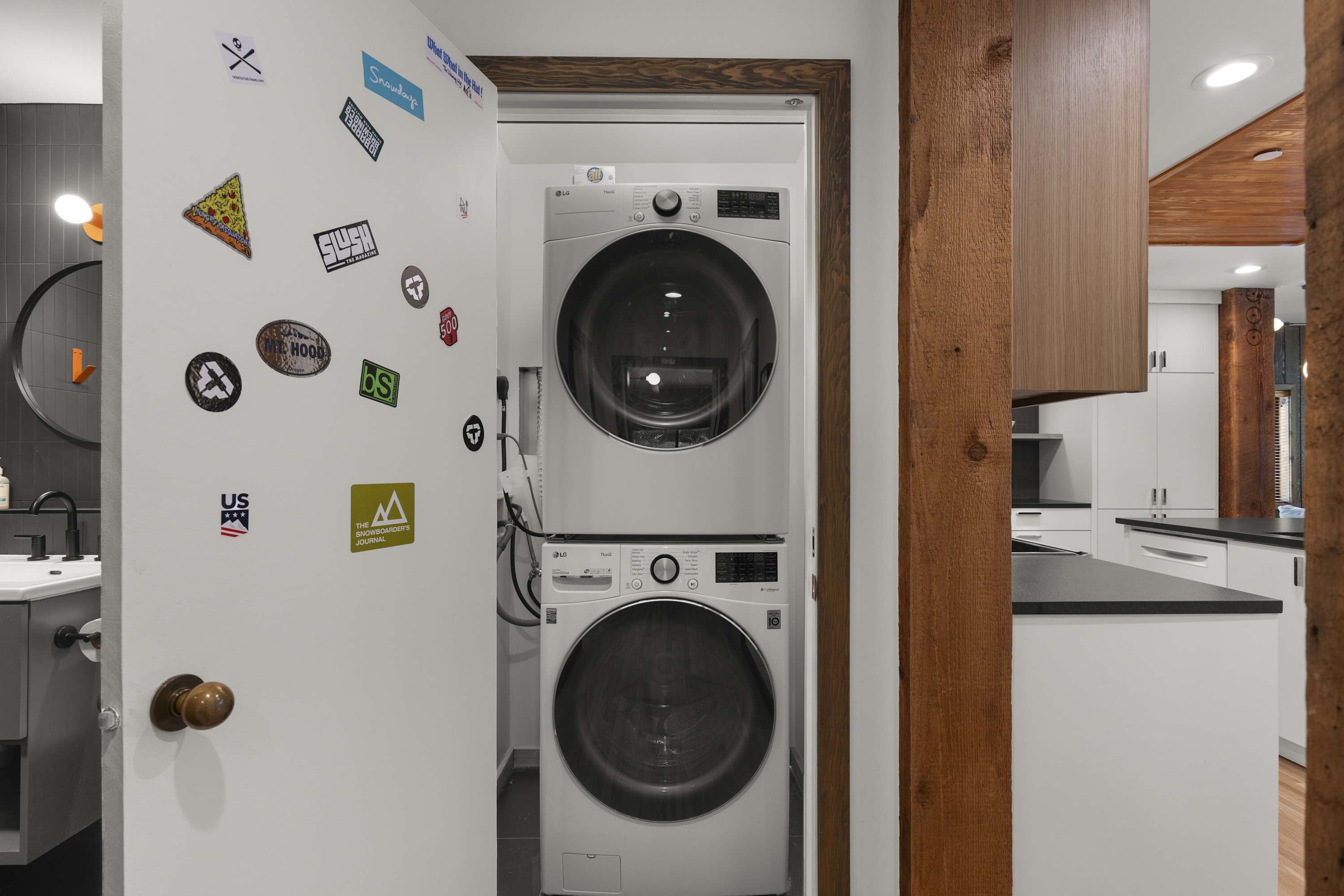 A laundry room with two stacked washing machines, a wooden door frame, and a white wall with various stickers.