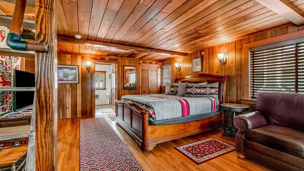 Een kamer met houten lambrisering, een bed, een lederen fauteuil en een kleine tafel.