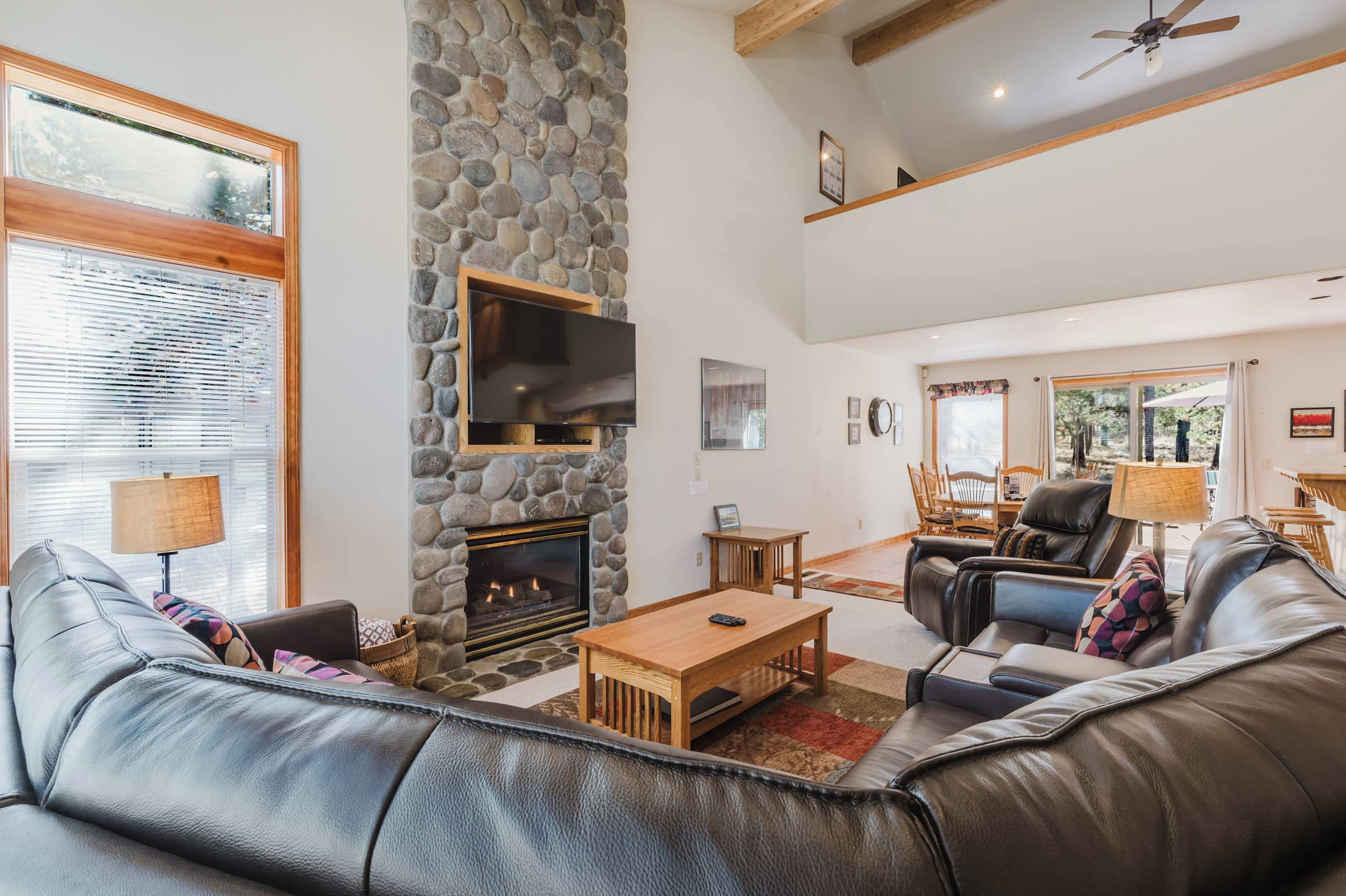 A spacious living room with a stone fireplace, leather sofas, a flat-screen TV, and a dining area with a table and chairs.