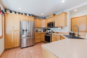 A modern kitchen with wooden cabinets, stainless steel appliances, and a tiled floor. - Sweet Sunriver Home with Private Hot Tub, Outdoor Space & Eight SHARC Passes (Sunriver)