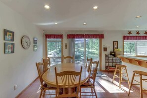 A dining area with a round table, wooden chairs, and a bar area with stools. - Sweet Sunriver Home with Private Hot Tub, Outdoor Space & Eight SHARC Passes (Sunriver)