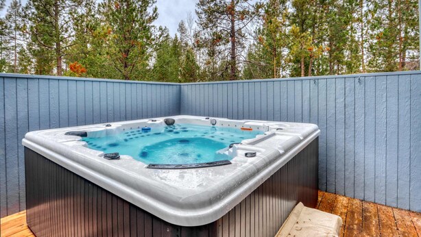 Un bain à remous installé dans un coin, avec une terrasse en bois et une clôture bleue.