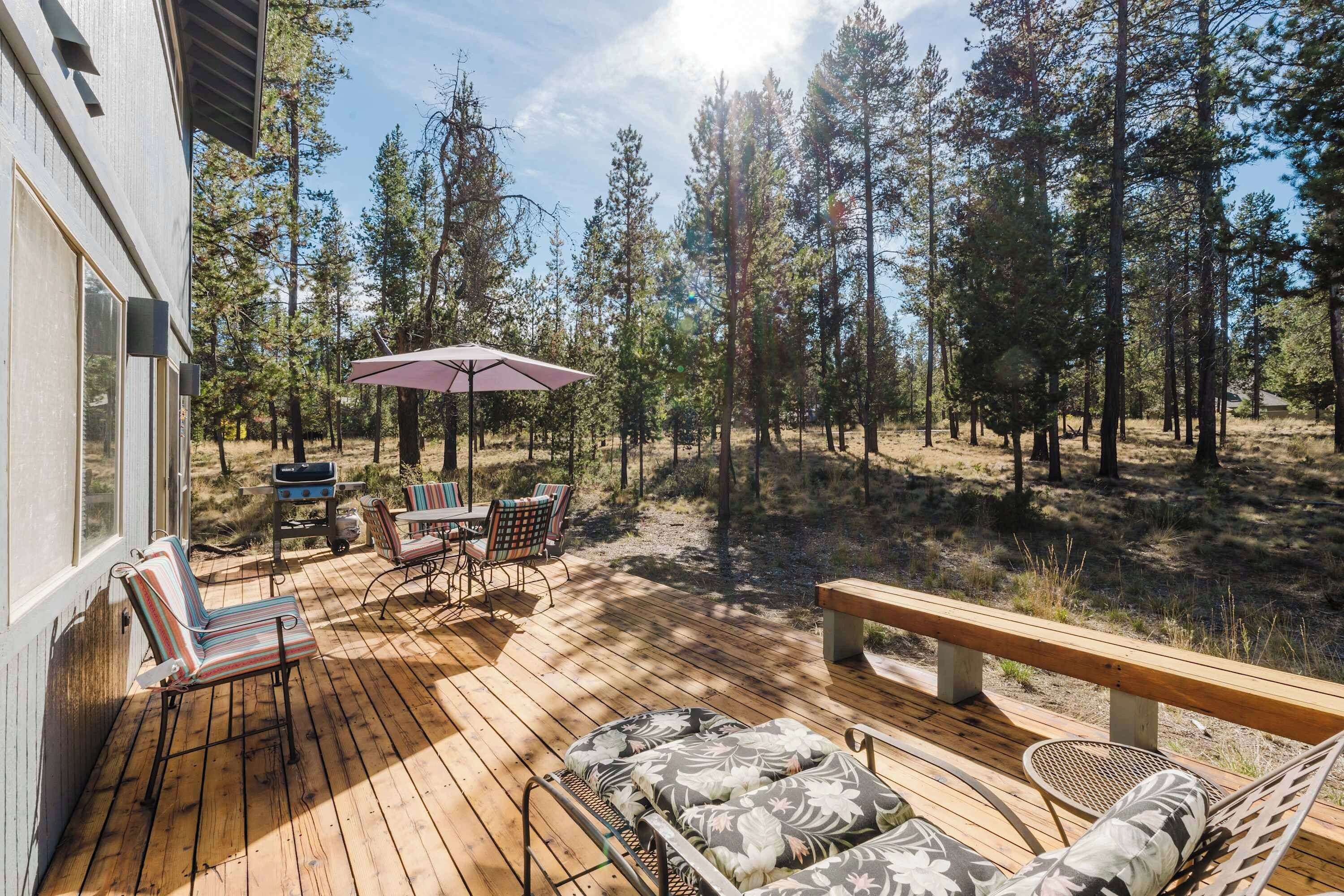 A wooden deck with outdoor furniture, a grill, and a view of a forested area.