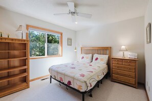 Un dormitorio con cama, mesita de noche, cómoda, ventana y ventilador de techo.