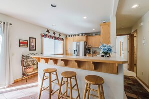 Una cocina con isla central, taburetes de madera y una ventana con persianas.