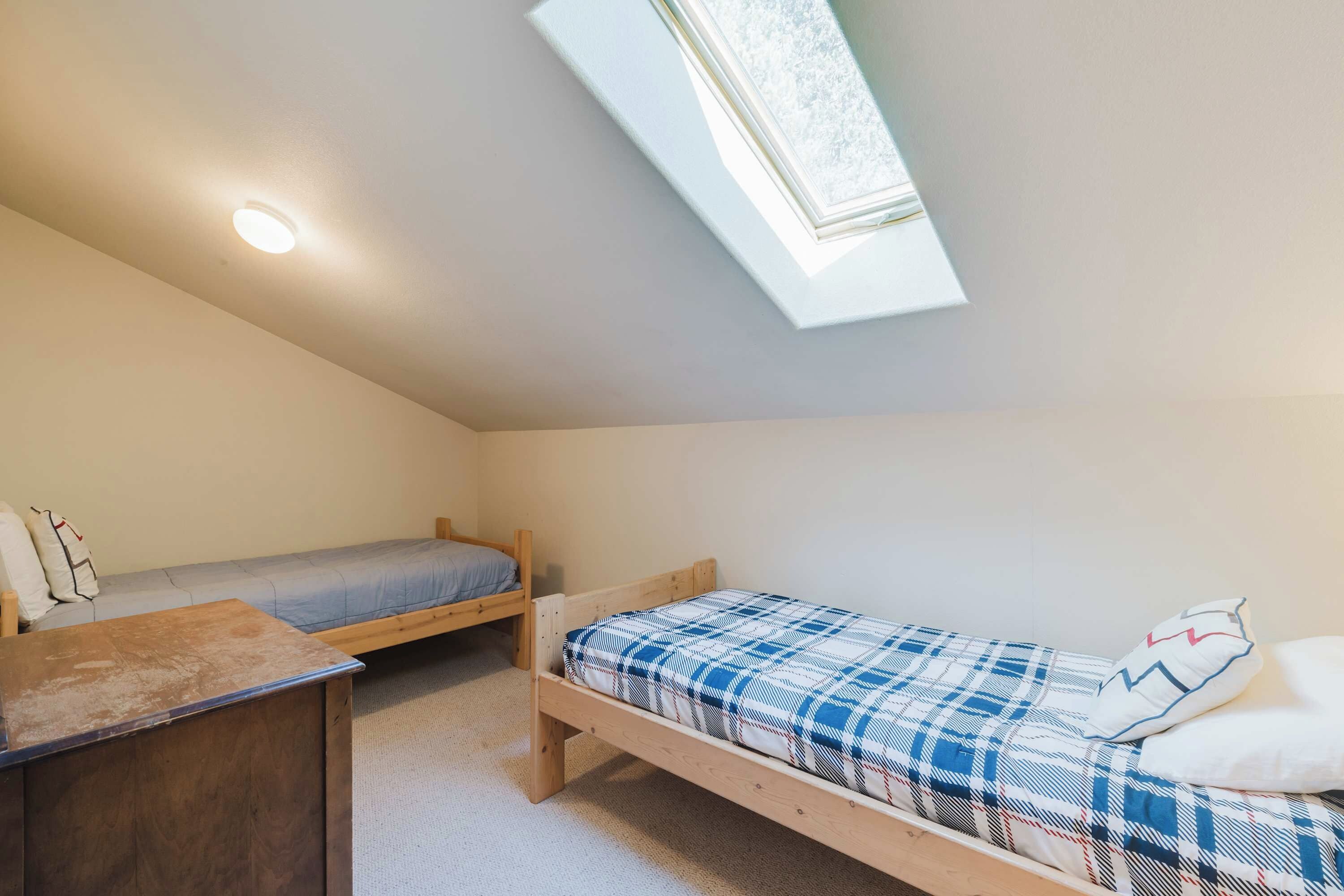 A small, single-room accommodation with a sloped ceiling, a skylight, and two wooden beds.