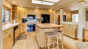 A modern kitchen with wooden cabinets, a central island with bar stools, a built-in oven, and a skylight.