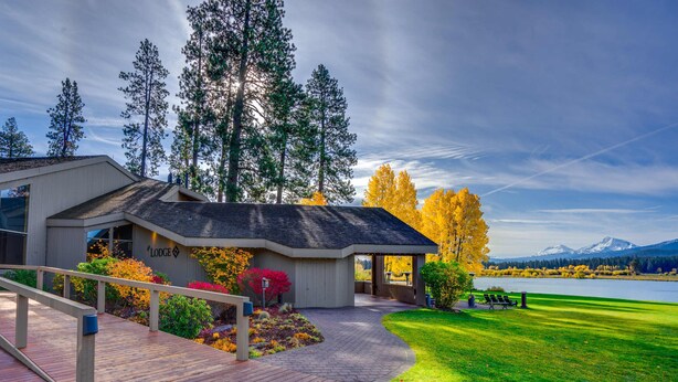 A lodge with a wooden deck, a covered patio, and a view of a lake and mountains.