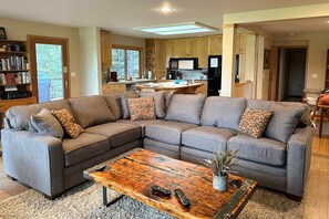 A modern living room with a sectional sofa, a wooden coffee table, and a kitchen in the background.