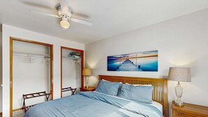 A bedroom with a bed, a ceiling fan, a nightstand with a lamp, a wooden headboard, a wall-mounted artwork, and a wardrobe with a mirror. - Delightful Home with Ocean View & Private Hot Tub - 3 Blocks to Beach (Yachats)