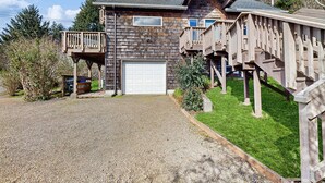 A wooden house with a garage, a covered porch, and a small deck. - Delightful Home with Ocean View & Private Hot Tub - 3 Blocks to Beach (Yachats)