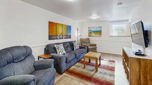 A living room with a sofa, armchair, coffee table, and TV stand. - Delightful Home with Ocean View & Private Hot Tub - 3 Blocks to Beach (Yachats)
