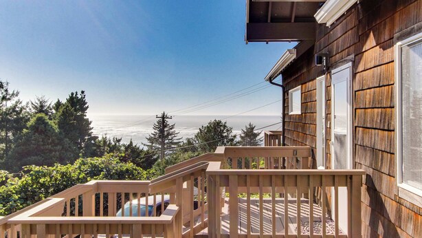 A wooden deck with a view of the ocean, a vehicle parked nearby, and a house with a visible window and door. - Delightful Home with Ocean View & Private Hot Tub - 3 Blocks to Beach (Yachats)