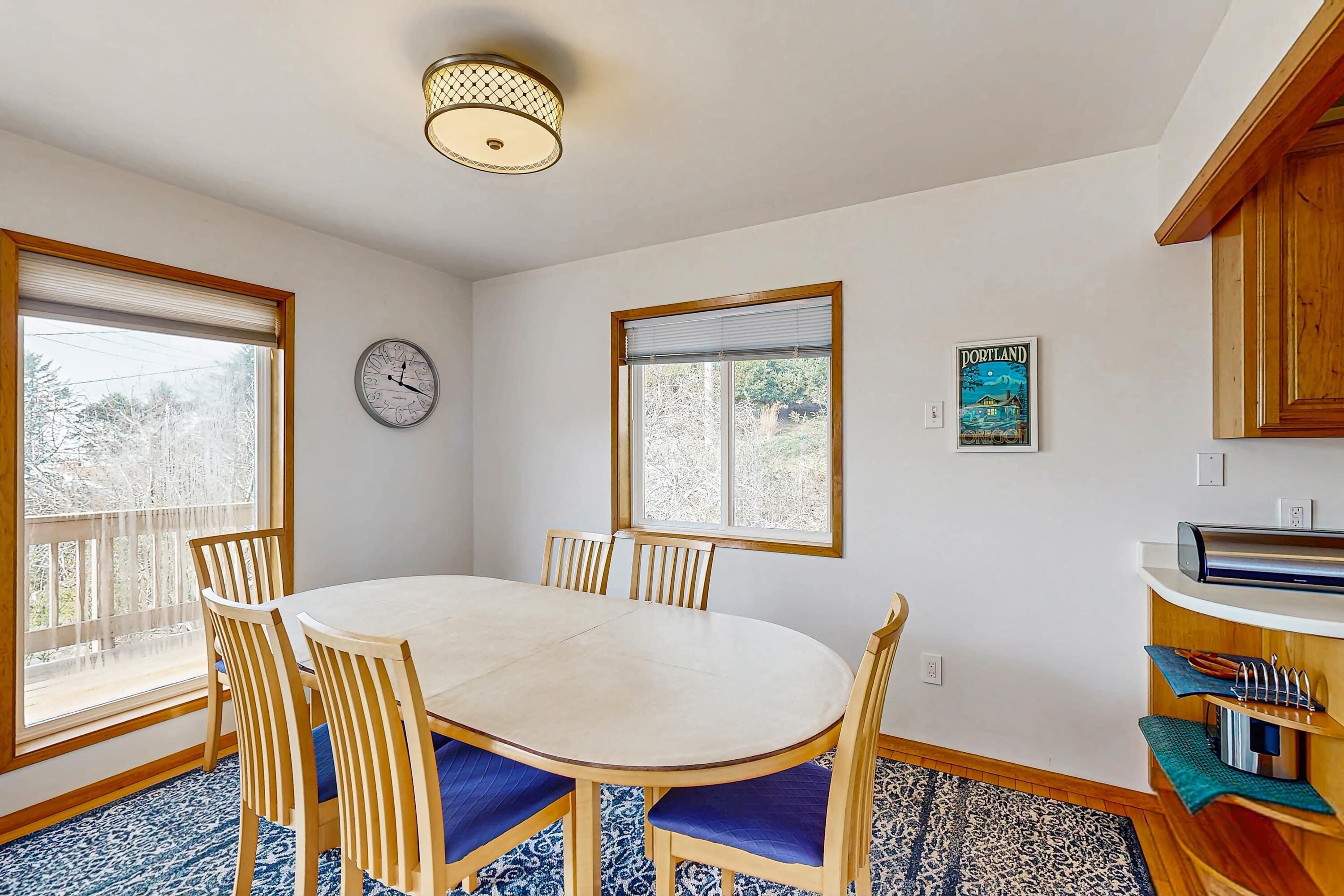 Un coin repas avec une table ronde, des chaises, une horloge et une fenêtre avec des stores.