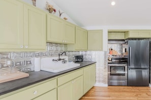A kitchen with green cabinets, a stainless steel refrigerator, and a patterned backsplash. - Cozy recreation home with full kitchen, washer & dryer, private lot and WIFI (Bend)