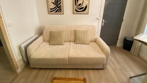 A room with a beige sofa, two wall-mounted abstract art pieces, a door, and a trash bin. - L'Echappé Médiévale in the heart of a small Alpine town (Veynes)