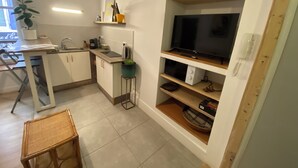 A compact kitchen with a dining area, a TV on a shelf, and a small table with chairs. - L'Echappé Médiévale in the heart of a small Alpine town (Veynes)
