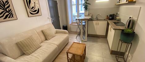 Un salon moderne avec un canapé, une petite table en bois et un coin cuisine comprenant un évier et des placards.