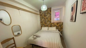A bedroom with a bed, a chair, a window with a view, and a mirror. - L'Echappé Médiévale in the heart of a small Alpine town (Veynes)