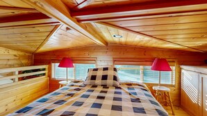 Een slaapkamer in een houten chalet met een geruit beddegoed, twee rode lampen en een raam met luiken.