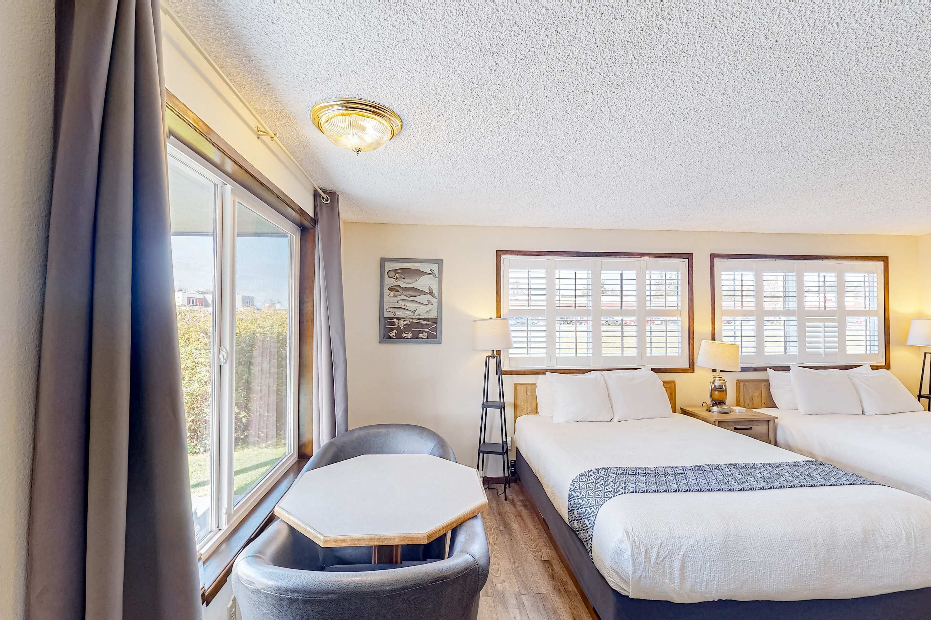 Una habitación de hotel con cama, escritorio, silla y dos ventanas con persianas.