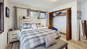 Een slaapkamer met een bed, nachtkastjes, een kledingkast en een raam met gordijnen.