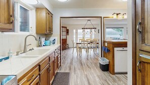 Een keuken met houten kastjes, een dubbele spoelbak en een eethoek met een tafel en stoelen.