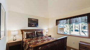 Un dormitorio con una cama de madera, dos mesitas de noche, una mesilla auxiliar, una ventana con vistas y un cuadro enmarcado en la pared.