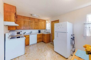 A compact kitchen with wooden cabinets, a white refrigerator, a microwave, and a washing machine.