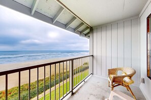 A balcony with a view of the ocean, a wicker chair, and a concrete floor. - Oceanfront condo with amazing view, fireplace, balcony & beach access (Newport)