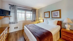 Habitación de hotel con cama, mesitas de noche, televisor, ventana con cortinas y dos cuadros en la pared.
