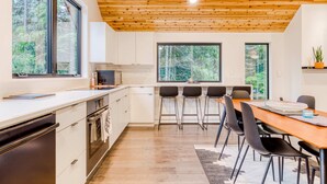 A modern kitchen with white cabinets, a wooden ceiling, and large windows.