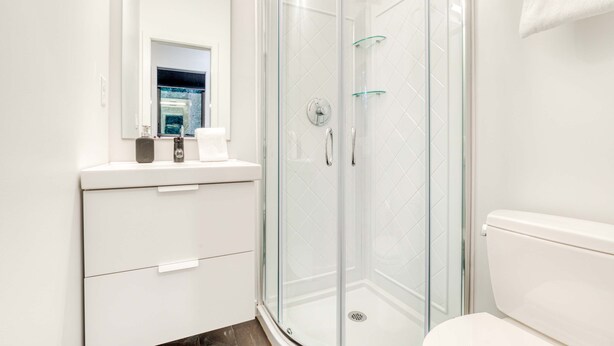 A modern bathroom with a glass-enclosed shower, a white toilet, and a vanity with a mirror. - Sleek, Modern Home in Town with Forest Views, Fire Table, WiFi - Walk to Skiing (Government Camp)