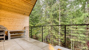An outdoor patio with a fire feature, a grill, and a view of a forest.
