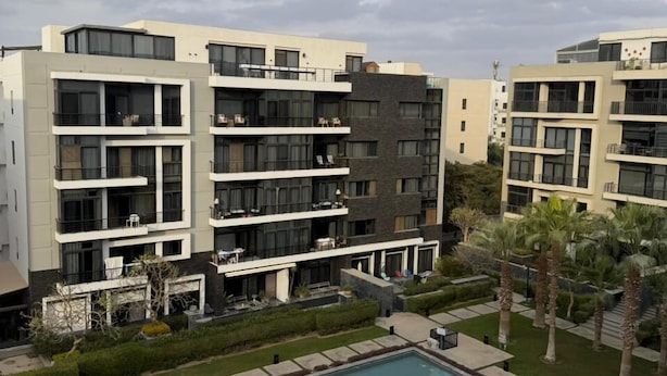 Un moderno edificio residencial de varios pisos, con balcones, un patio central y una piscina.