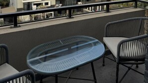 Un balcón con una mesa y sillas de vidrio, con vista a un conjunto de edificios de apartamentos modernos.