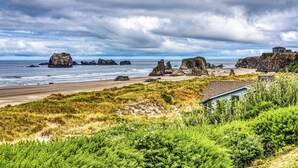 A coastal landscape with rocky outcrops, a beach, and a house on a cliff overlooking the ocean.