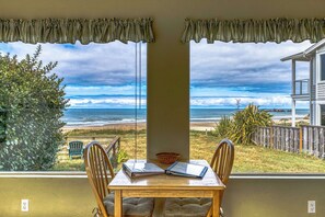 A room with a table and chairs facing a beach view through large windows. - Inviting dog-friendly studio with unobstructed ocean views (Bandon)