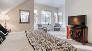 A bedroom with a bed, a television on a wooden cabinet, and two chairs in a corner. - Golf course-view townhome with private hot tub & SHARC access (Sunriver)