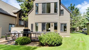 A two-story house with a deck, outdoor seating, and a well-maintained lawn. - Golf course-view townhome with private hot tub & SHARC access (Sunriver)