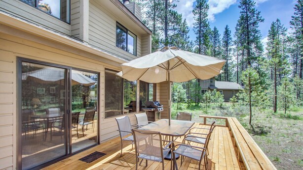 A wooden deck with a glass door leading to an outdoor dining area, a barbecue grill, and a large umbrella. - Cabin with Private Hot Tub Near the Deschutes River - Free SHARC access (Sunriver)