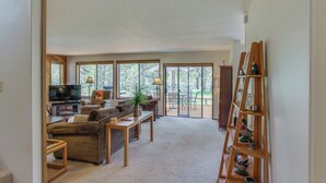 A living room with a sofa, coffee table, TV, and a wooden ladder shelf. - Cabin with Private Hot Tub Near the Deschutes River - Free SHARC access (Sunriver)