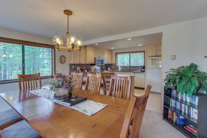 A modern kitchen with wooden cabinets, a dining table with chairs, a chandelier, and a bookshelf.