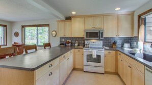 A kitchen with wooden cabinets, a microwave, an oven, and a large island with a sink. - Cabin with Private Hot Tub Near the Deschutes River - Free SHARC access (Sunriver)