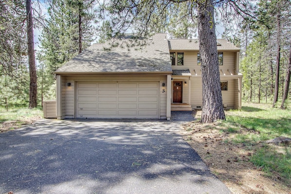A two-story house with a garage, surrounded by trees.