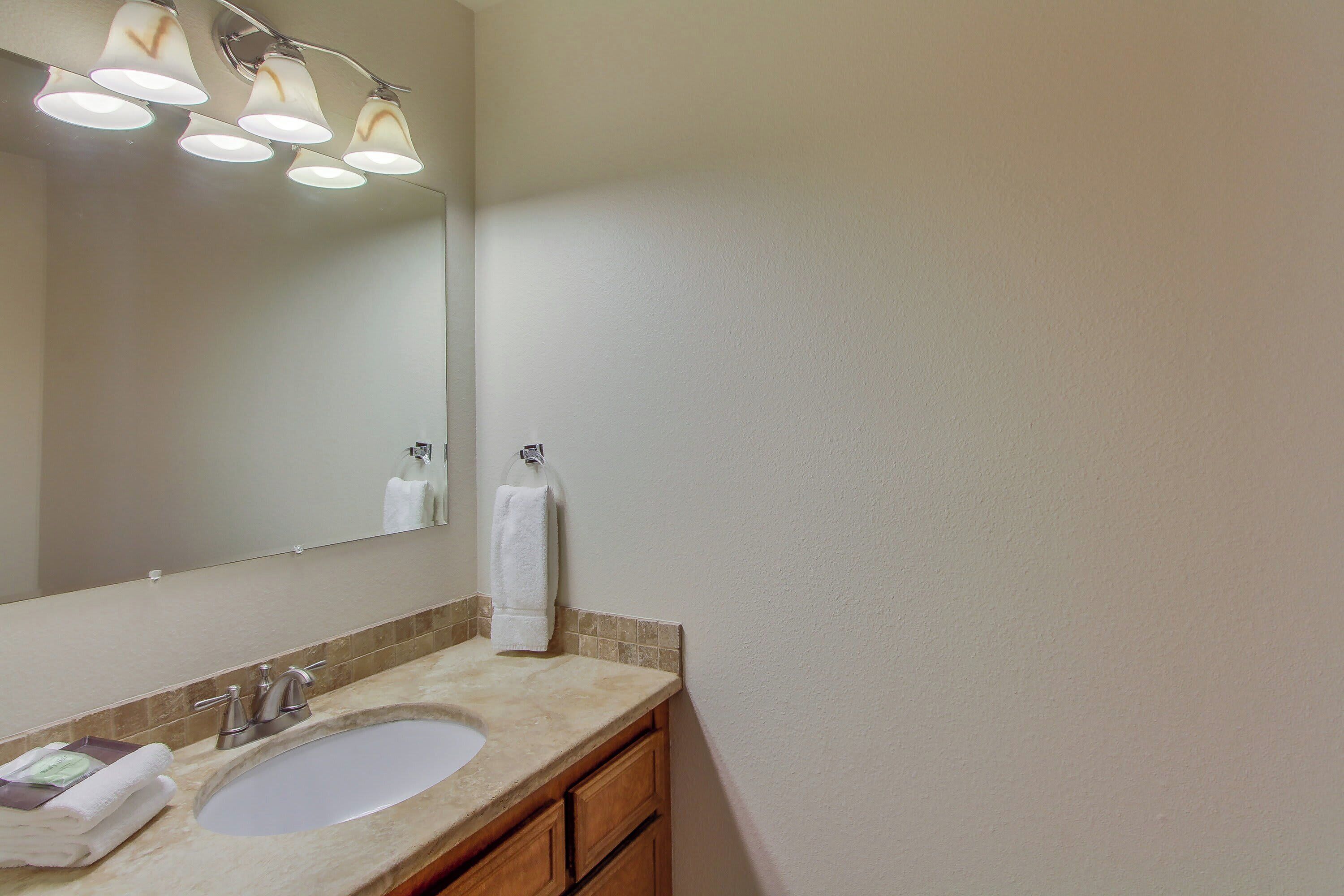 A bathroom with a sink, mirror, towel rack, and three overhead lights.