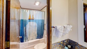 A bathroom with a bathtub, a toilet, a shower curtain with a nautical theme, and a tiled wall with a 'Makeup' sign. - Retro beach suite with  fast WiFI - walkable to downtown hot spots (Bandon)