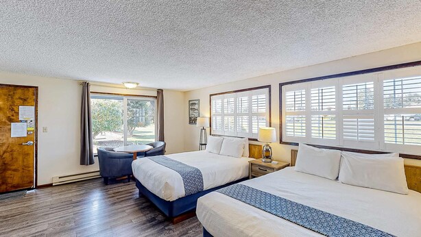 A hotel room with two beds, a desk, a chair, and large windows. - Retro beach suite with  fast WiFI - walkable to downtown hot spots (Bandon)