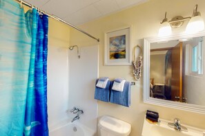Un baño con bañera, inodoro, lavamanos y espejo.